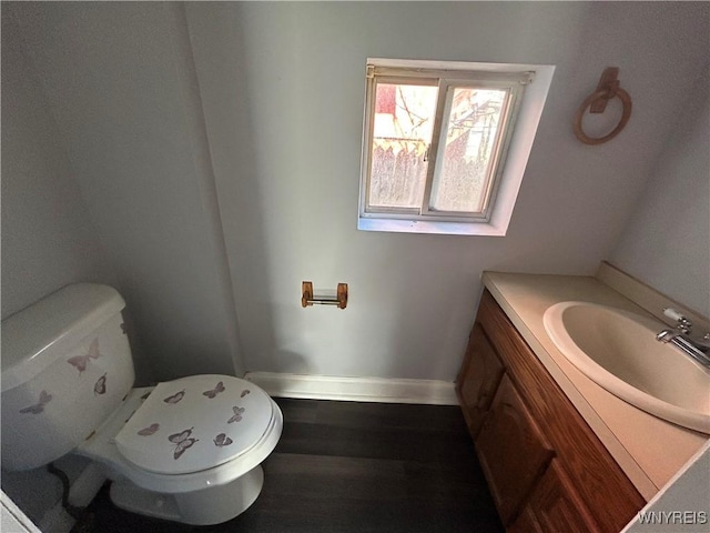 half bathroom with toilet, vanity, baseboards, and wood finished floors