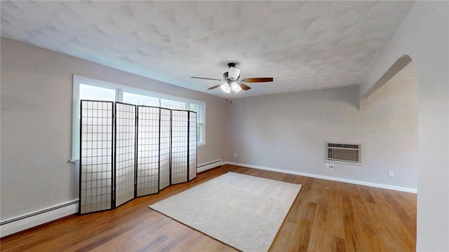 spare room with ceiling fan, wood finished floors, a wall unit AC, and a baseboard radiator
