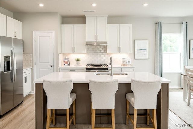 kitchen featuring visible vents, a center island with sink, a sink, under cabinet range hood, and stainless steel appliances