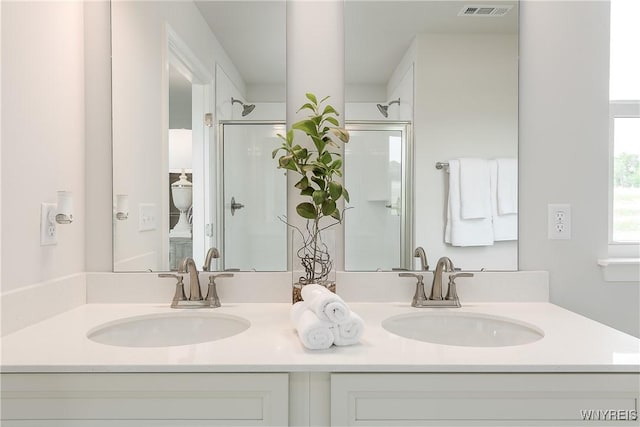 full bath featuring double vanity, a shower with shower door, visible vents, and a sink
