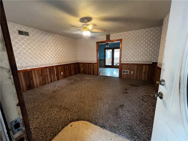 carpeted spare room with visible vents, wainscoting, wallpapered walls, and a ceiling fan