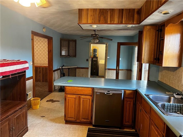 kitchen featuring a wainscoted wall, light floors, dishwasher, a peninsula, and a sink