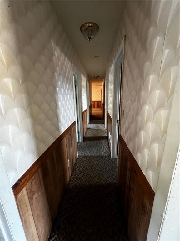 hall featuring dark carpet and wallpapered walls