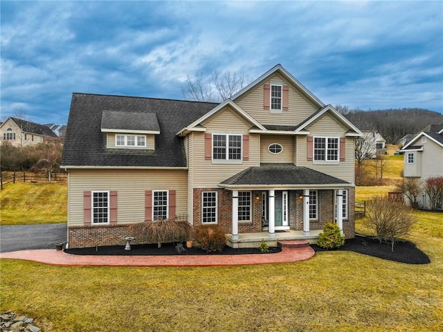 traditional-style home featuring brick siding, a front lawn, fence, roof with shingles, and covered porch