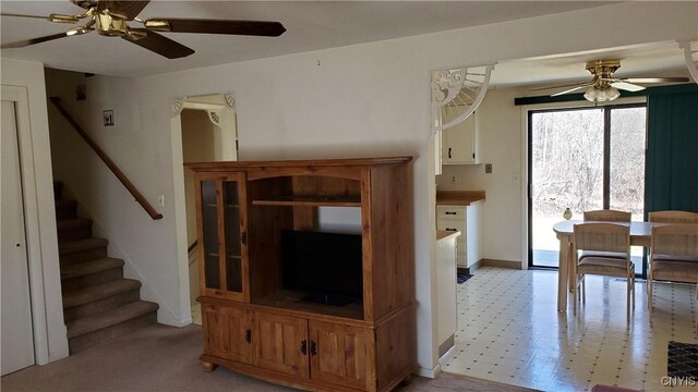unfurnished living room featuring stairway, a ceiling fan, and baseboards