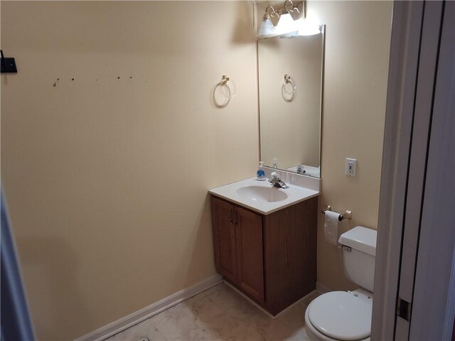 half bathroom with toilet, vanity, marble finish floor, and baseboards