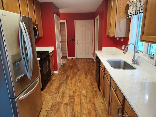 kitchen with black appliances, wood finished floors, brown cabinets, and a sink