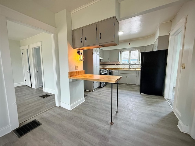 kitchen featuring visible vents, gray cabinets, freestanding refrigerator, a sink, and light wood-style floors