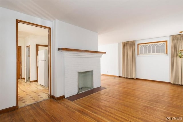 unfurnished living room featuring a brick fireplace, baseboards, and wood finished floors