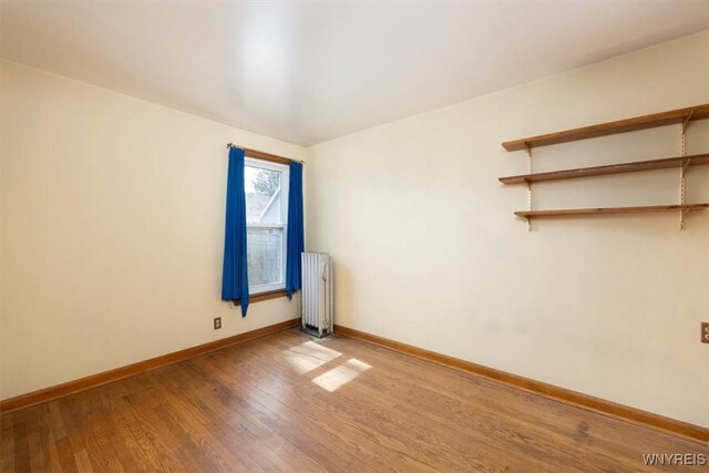 empty room featuring baseboards, radiator, and wood finished floors