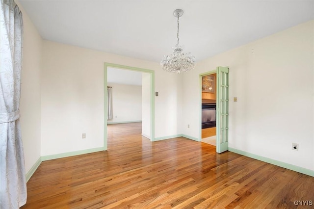 unfurnished room with a notable chandelier, light wood-style flooring, and baseboards