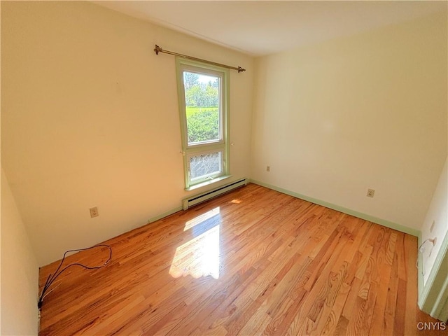 unfurnished room featuring a baseboard heating unit, light wood-style floors, and baseboards