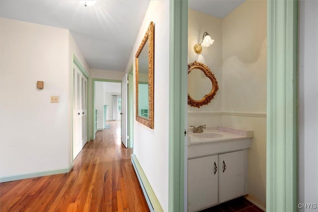 hallway featuring baseboards, wood finished floors, a baseboard radiator, and a sink
