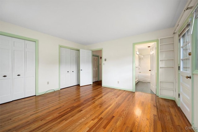 unfurnished bedroom featuring baseboards, multiple closets, ensuite bath, and light wood-style flooring