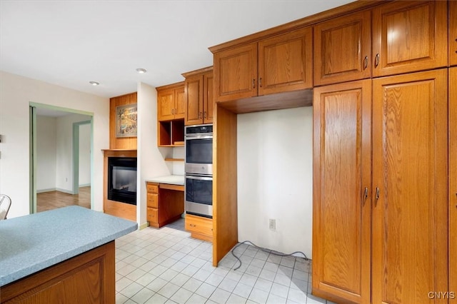 kitchen featuring open shelves, stainless steel double oven, brown cabinetry, light countertops, and a multi sided fireplace