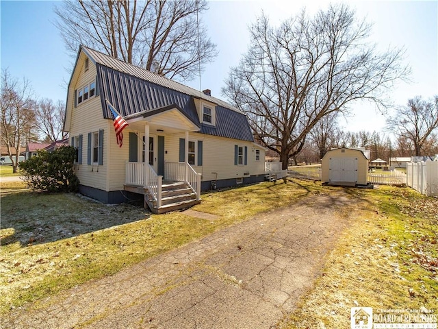 colonial inspired home with fence, a shed, a gambrel roof, an outdoor structure, and metal roof