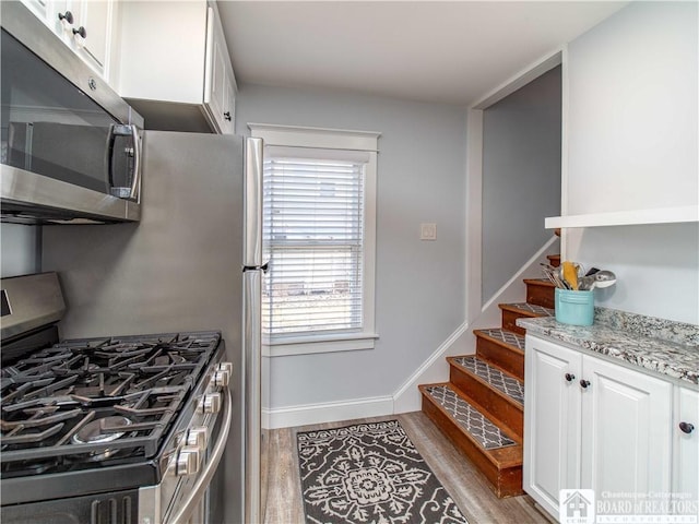 kitchen with light stone counters, wood finished floors, white cabinetry, appliances with stainless steel finishes, and baseboards
