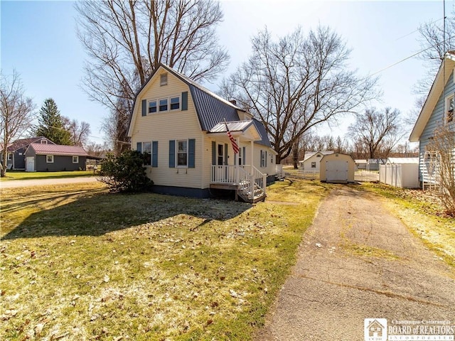 view of front of house with a gambrel roof, an outbuilding, driveway, a front lawn, and metal roof