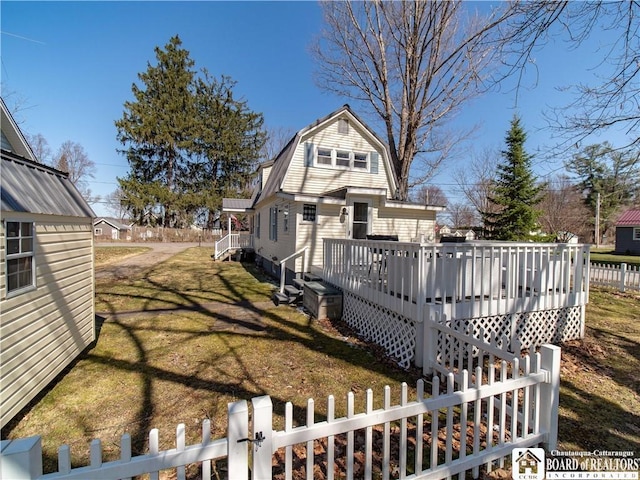 back of house with a fenced front yard, a gambrel roof, a lawn, and a deck