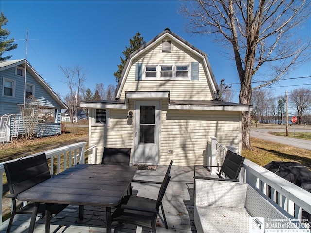 back of property with a deck, outdoor dining area, and a gambrel roof