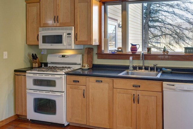 kitchen featuring a sink, light brown cabinetry, baseboards, white appliances, and dark countertops