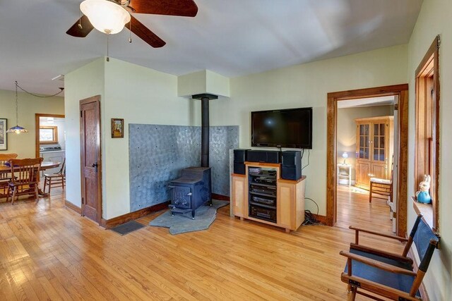 living room with baseboards, light wood-type flooring, a wood stove, and a ceiling fan