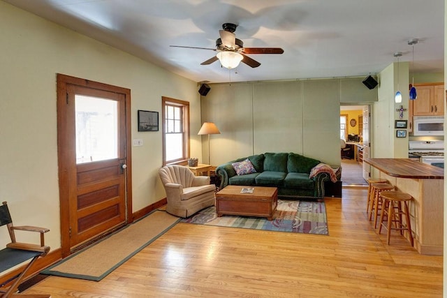 living room featuring baseboards, visible vents, light wood-style floors, and a ceiling fan