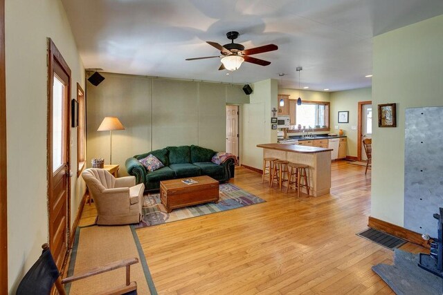 living area featuring light wood finished floors, baseboards, visible vents, and ceiling fan