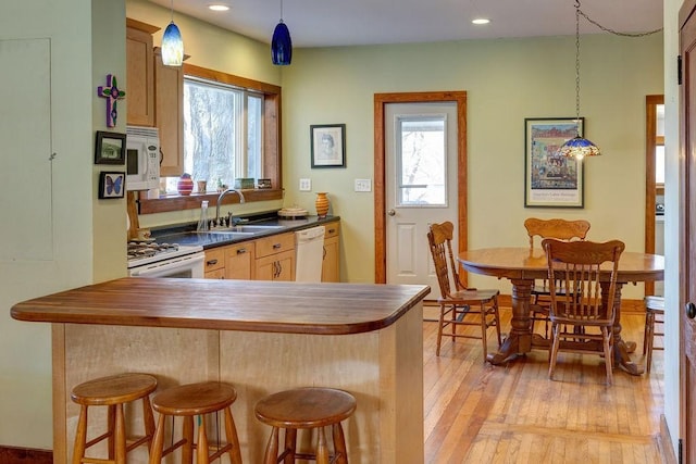 kitchen with white appliances, dark countertops, a sink, light wood-type flooring, and a breakfast bar area
