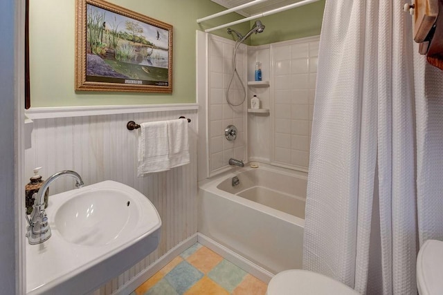 bathroom featuring a sink, shower / tub combo with curtain, toilet, and wainscoting