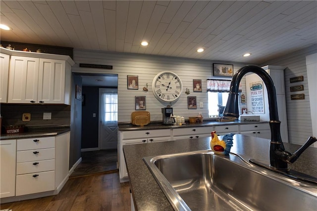 kitchen featuring dark countertops, dark wood-type flooring, wooden ceiling, white cabinets, and a sink