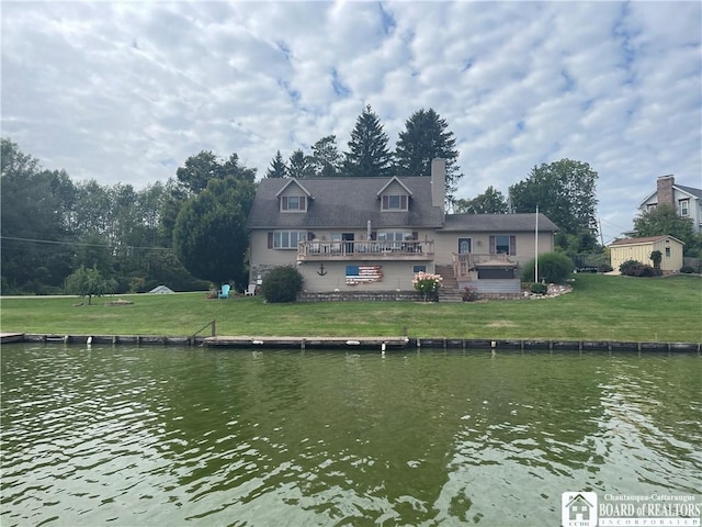 back of property with a chimney, a deck with water view, and a lawn