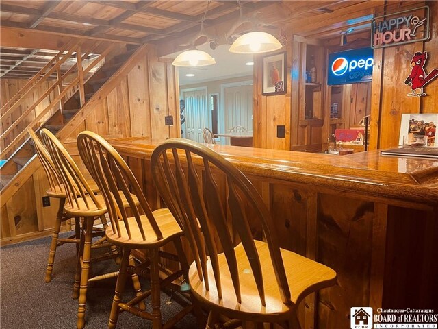 bar featuring carpet flooring, wood walls, bar, and stairway