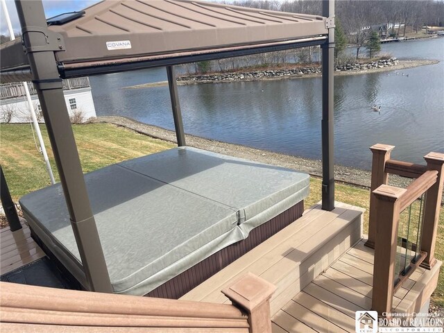 view of dock with a covered hot tub, a water view, and a yard
