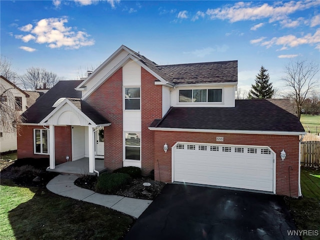 traditional-style home with driveway, fence, roof with shingles, a garage, and brick siding