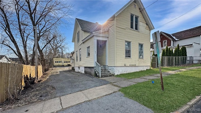 traditional-style home with entry steps, driveway, a front lawn, and fence