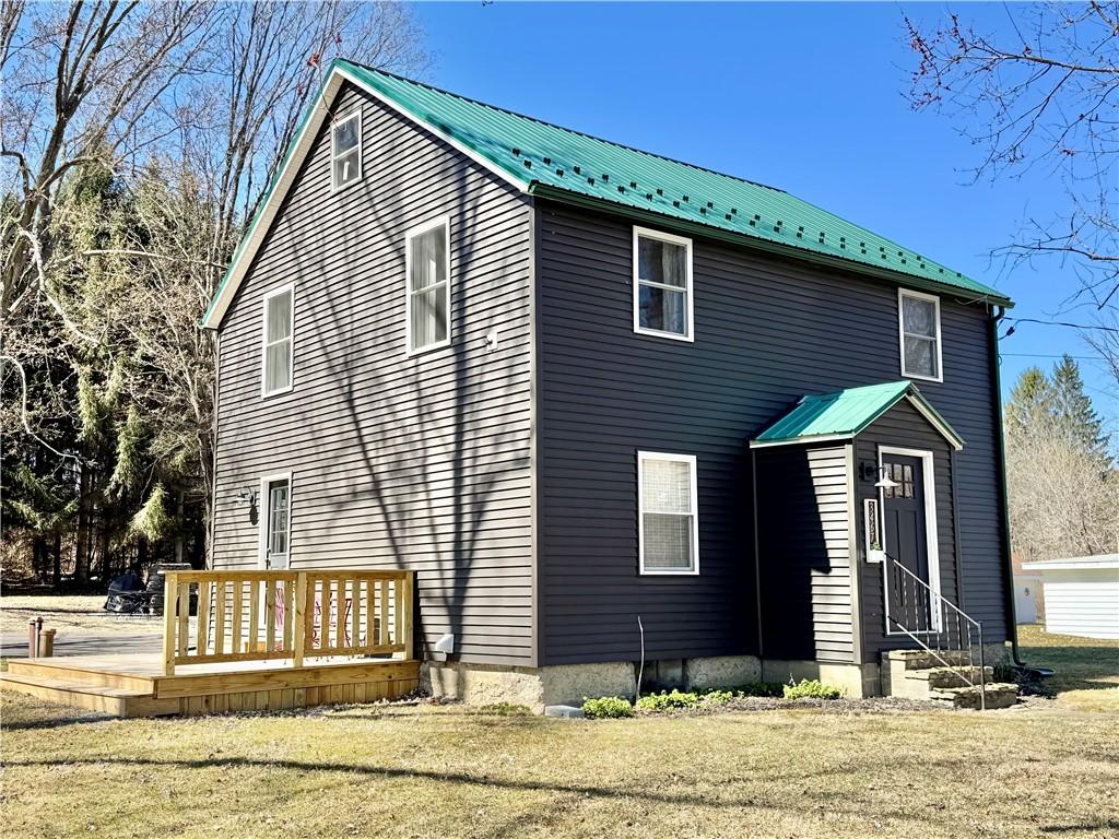view of front of home with entry steps, a front lawn, a wooden deck, and metal roof