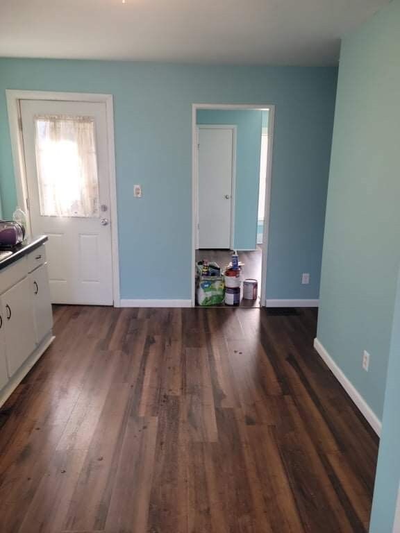 unfurnished dining area with baseboards and dark wood-style flooring