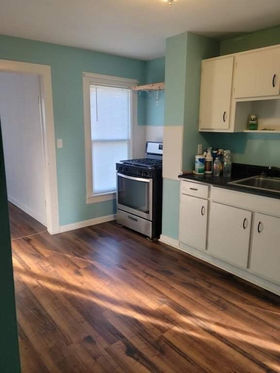 kitchen with white cabinets, dark countertops, stainless steel range with gas cooktop, a sink, and dark wood-style floors