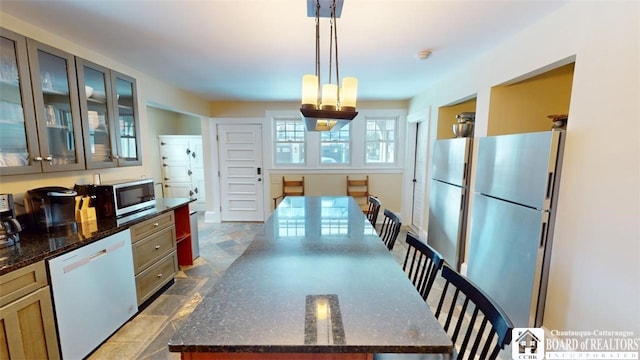 kitchen with hanging light fixtures, appliances with stainless steel finishes, stone finish floor, dark stone counters, and glass insert cabinets