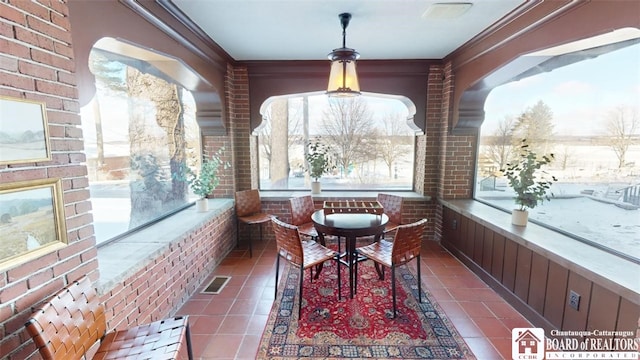 tiled dining room featuring brick wall, visible vents, ornamental molding, and a wealth of natural light