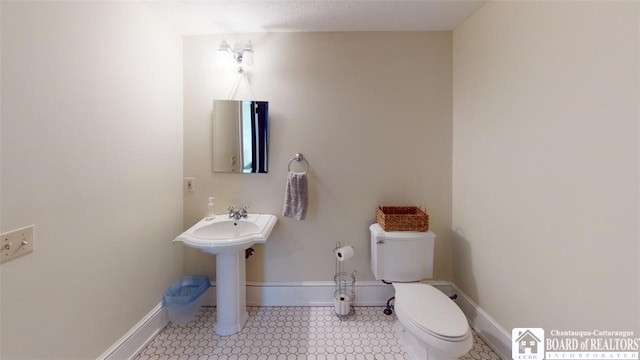 bathroom featuring toilet, baseboards, a sink, and tile patterned floors