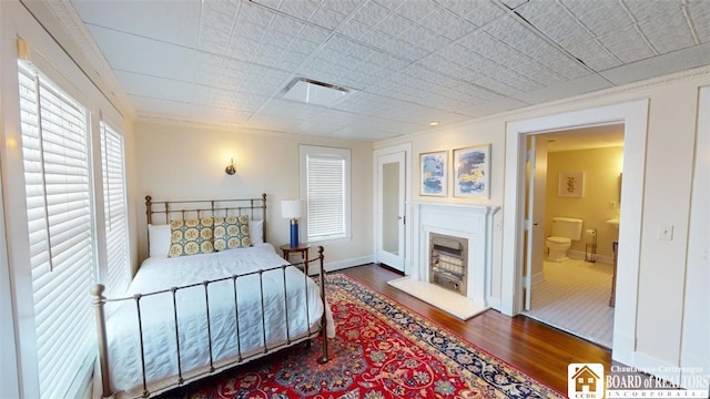 bedroom with baseboards, connected bathroom, wood finished floors, and a premium fireplace
