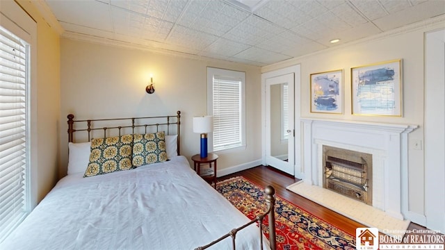 bedroom featuring dark wood-style flooring, baseboards, ornamental molding, and a fireplace
