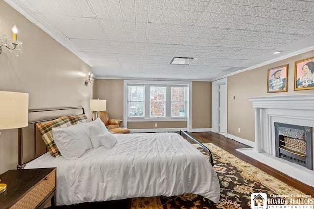 bedroom featuring baseboards, ornamental molding, wood finished floors, and a fireplace