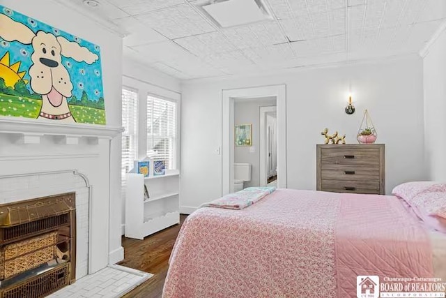 bedroom with a fireplace with flush hearth, ornamental molding, and wood finished floors