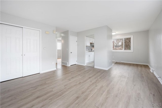 unfurnished bedroom with a closet, baseboards, light wood-style floors, and visible vents