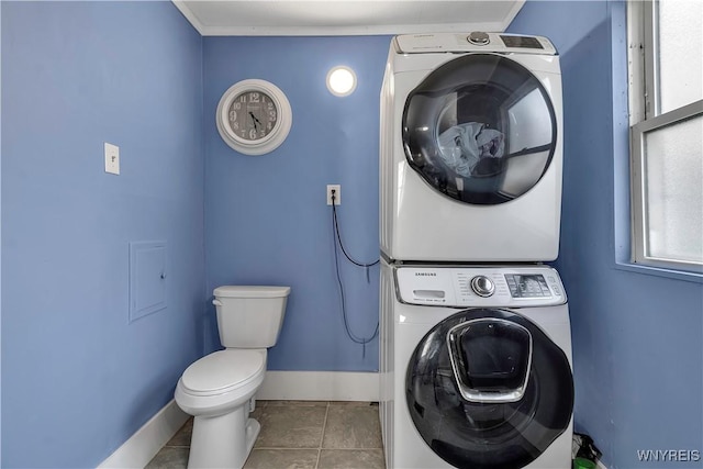 bathroom with baseboards, stacked washer and clothes dryer, tile patterned flooring, and toilet