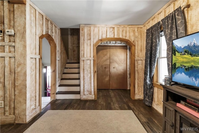 foyer with dark wood-type flooring, arched walkways, wood walls, and stairway
