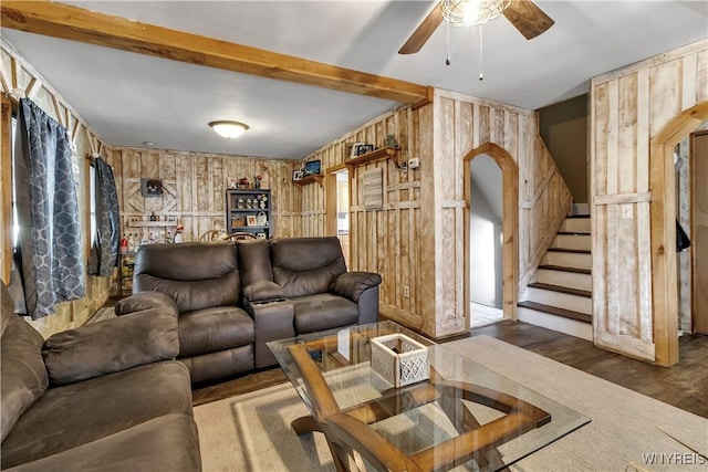 living room with a ceiling fan, arched walkways, wooden walls, and stairway